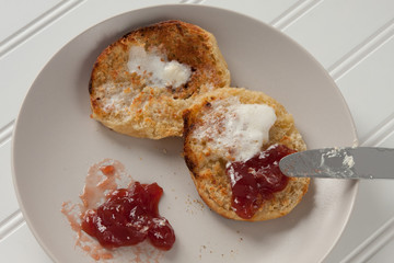Split and toasted English muffin with butter and strawberry jam on a plate