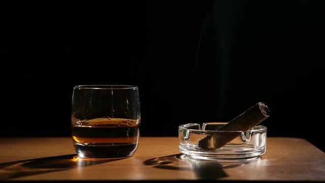Glass of whiskey with smoking cigar.Glass of alcohol and smoking noble cigar on a black background.