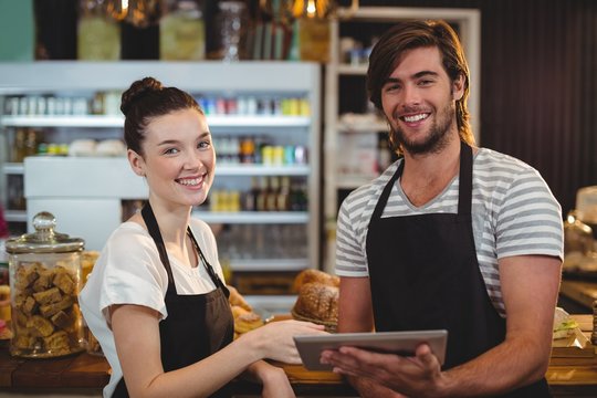 Smiling waiter and waitress using digital tablet at counter