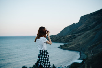 Woman sitting by the sea in the mountains with a camera
