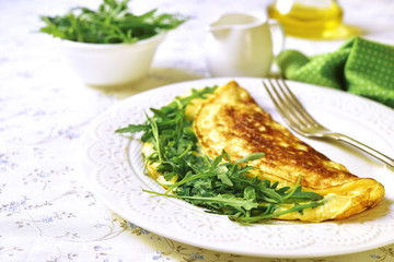 Omelet with cheese and arugula on a white plate.