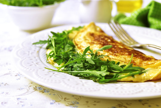 Omelet with cheese and arugula on a white plate.