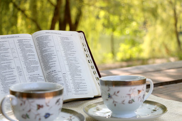 open book, two design cups of coffee on the wooden table in sunny day in the forest 