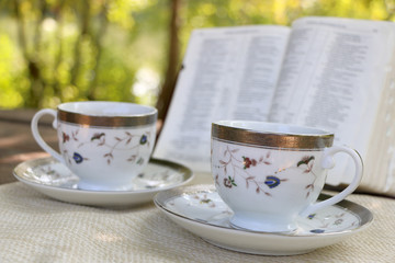  open book, two design cups of coffee on the wooden table in sunny day in the forest 