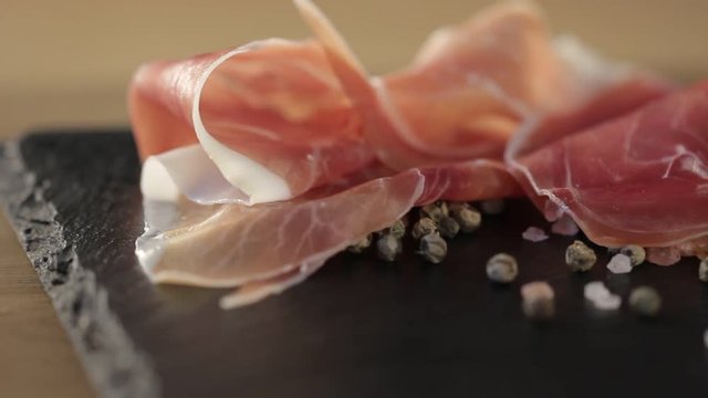 Thin slices of pork ham on the wood plate. Dolly shot. Closeup