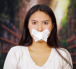 Young brunette woman tied up with rope around wrists and white tape covering mouth, facing camera,...