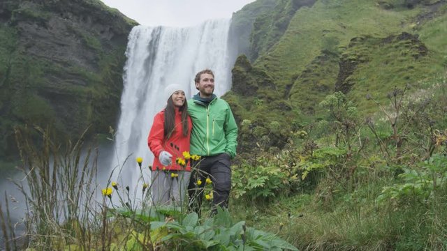 Hiking travel couple by waterfall on Iceland outdoors  Skogafoss. People visiting famous tourist attractions and landmarks in Icelandic nature landscape on the ring road. RED EPIC SLOW MOTION.
