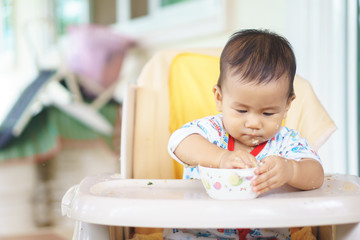 Asian baby eating food by himself