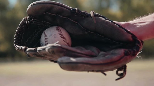 Slowmotion Close Up of Man Wearing Baseball Glove and Tossing Baseball from Hand to Hand During Baseball Game Outdoors in Field on Sunny Day in Summer.