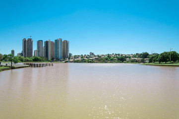 Fototapeta na wymiar Park pond with city background and blue sky. Sunny day, landscape in a horizontal photo.