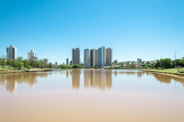 Obraz na płótnie Canvas A beautiful sunny day at the lake with buildings and the city background. Scene reflected on water. Landscape from Park of Indigenous Nations in the city of Campo Grande MS, Brazil.