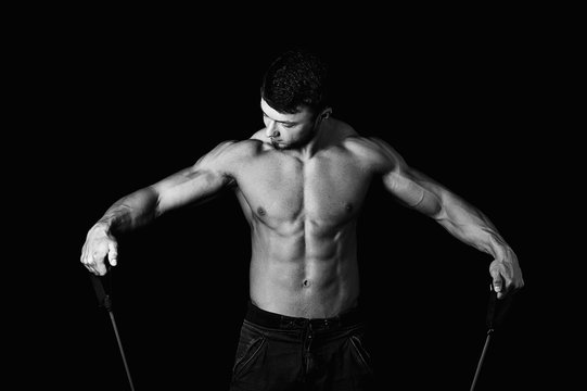 Young muscular man is engaged with the expander .Studio on a dark background , a black and white image