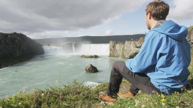 Iceland tourist relaxing by waterfall Godafoss. Man hiker resting on travel visiting tourist attractions and landmarks in Icelandic nature on Ring Road, Route 1. RED EPIC SLOW MOTION.