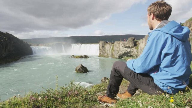 Hiker relaxing hiking - waterfall Godafoss Iceland. Man hiker resting on travel visiting tourist attractions and landmarks in Icelandic nature on Ring Road, Route 1.