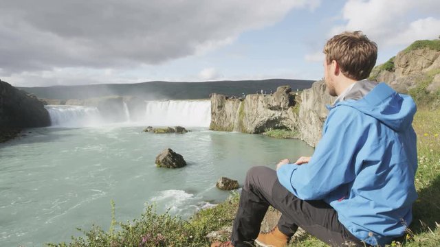 Hiking Iceland tourist at waterfall Godafoss. Man hiker resting on travel visiting tourist attractions and landmarks in Icelandic nature on Ring Road, Route 1. RED EPIC SLOW MOTION.