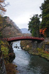 Ancient Japanese red arc bridge crossing creek surrounded by Aut