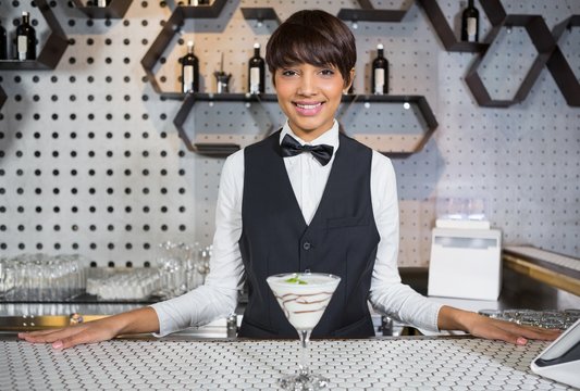 Waitress standing in bar counter with glass of cocktail