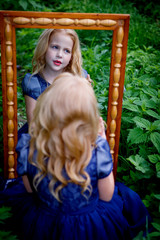 Portrait of beautiful little girl in the blue dress in nature with a mirror