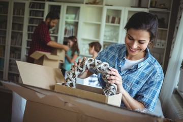 Woman unpacking cartons while family standing in background - obrazy, fototapety, plakaty