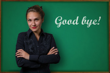 Beautiful young woman teacher (student, business woman) in classical dress standing near a blackboard with the inscription good bye