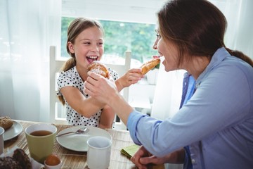 Mom & daughter feeding croissant to each other 