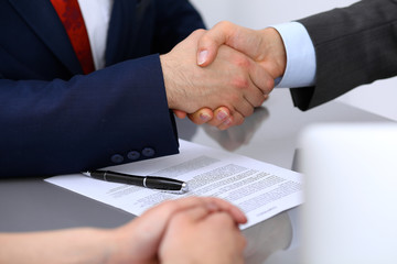 Two business man shaking hands to each other above signed contract