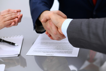 Two business man shaking hands to each other above signed contract