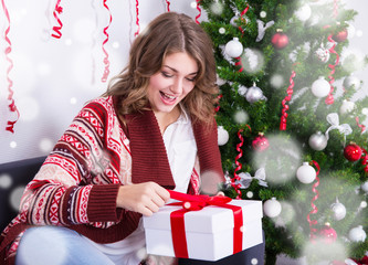 cheerful young woman opening christmas gift near christmas tree