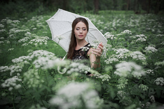 Portrait of beautiful girl with umbrella in nature and white flowers