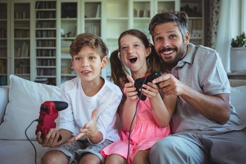 Father sitting on sofa with his children and playing video games