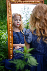 Portrait of beautiful little girl in the blue dress in nature with a mirror