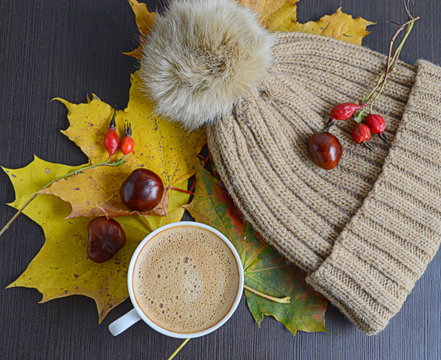 Cup of coffee with leaves, chestnuts and faux fur pompon hat