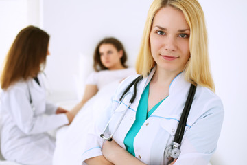 Young beautiful female doctor smiling  on the background with patient and his physician in hospital. High level and quality medical service concept.