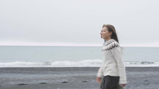 Iceland couple wearing Icelandic sweaters on black sand beach. Woman and man model in typical Icelandic sweater looking at ocean enjoying view of nature landscape at ocean sea. 60 FPS RED EPIC.