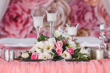 wedding table decorated with fresh flowers, candles and silver cups. Paper flowers in the background