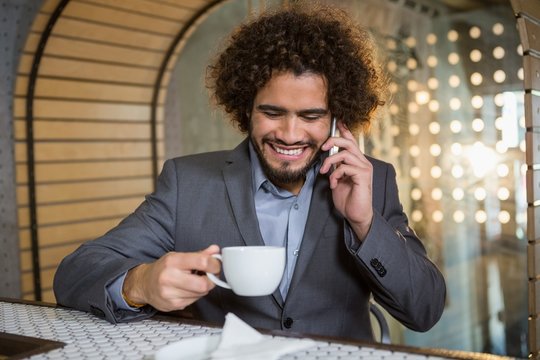 Businessman talking on mobile phone while having cup of tea