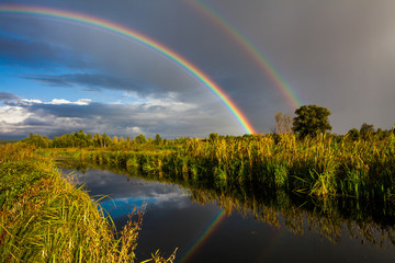 Fototapeta na wymiar Amazing double rainbow over the small rural river.