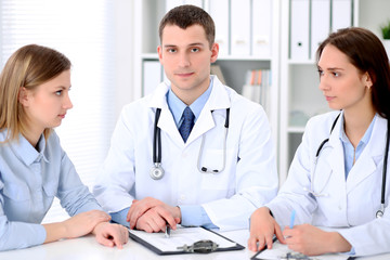 Two doctors  and  patient sitting at the table in medical cabinet.  High level and quality medical service concept.