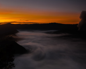 Fototapeta na wymiar The fog creeps over the water under an orange sky (Bohorok, Indonesia)