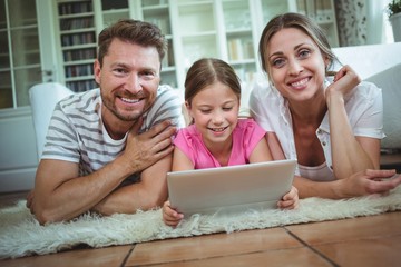 Parents and daughter lying on rug and using digital tablet