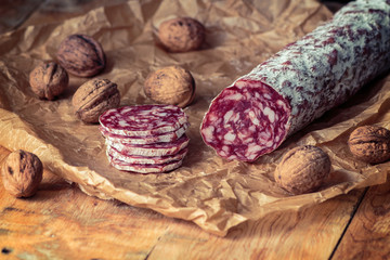 Italian salami with walnuts on craft paper on rustic  wooden background.