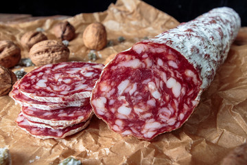 Italian salami with walnuts on craft paper on rustic  wooden background.