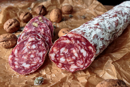 Italian salami with walnuts on craft paper on rustic  wooden background.