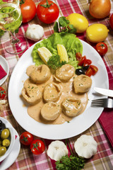 Salmon tortellini in sauce served on a white plate with lemon, olives, cherry tomatoes and parsley next to fresh garlic and tomatoes.