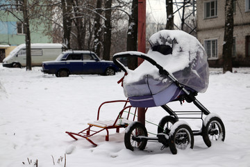 Baby stroller full of snow in the yard in a winter day