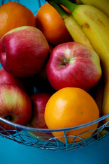 Metal fruit bowl on a wooden surface. Close. Bananas, oranges apples