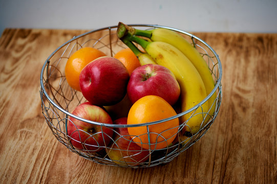Metal fruit bowl on a wooden surface. Close. Bananas, oranges apples