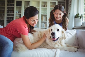 Mother and daughter sitting with pet dog in living room