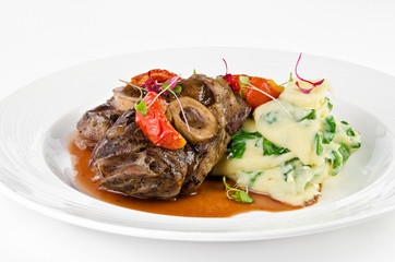 Braised beef on the bone with dried tomatoes and mashed potatoes with spinach and feta cheese on a plate on a white background, closeup