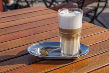 Ein Glas mit Latte Macchiato auf einem kleinen Silbertablett mit einem kleinen runden Keks